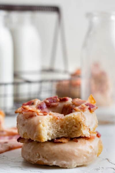 two maple bacon dnouts stacked with a bite taken out of the top one