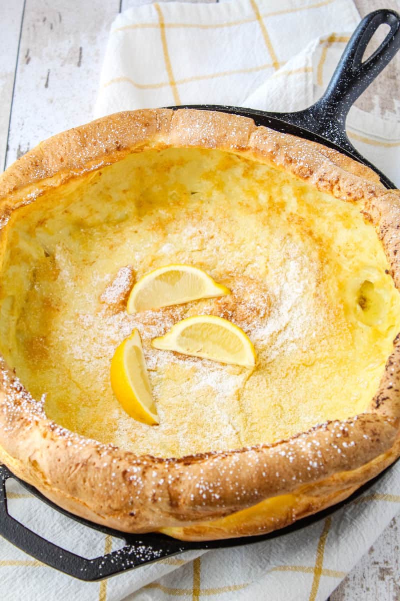 whole german pancake in a cast iron skillet with powdered sugar and lemon wedges