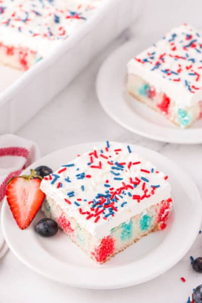 slices of 4th of juliy poke cake on plates with strawberries and blueberries