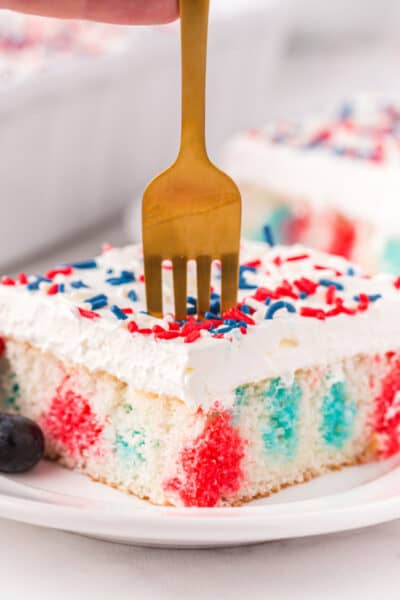 slice of 4th of july poke cake on a plate with a fork stuck into the top