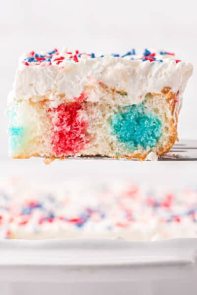 slice of 4th of july poke cake on a spatula over the pan to show colors inside