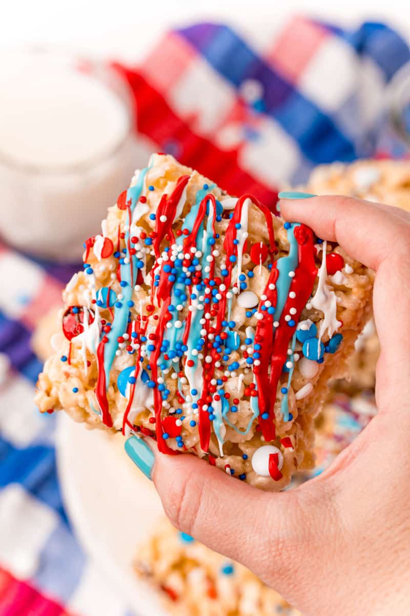 hand holding a 4th of july rice krispie treats with red, white, and blue candy melts drizzled on top
