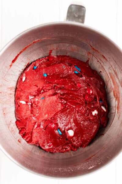 red velvet cake mix cookie dough in a mixing bowl with M7Ms mixed in