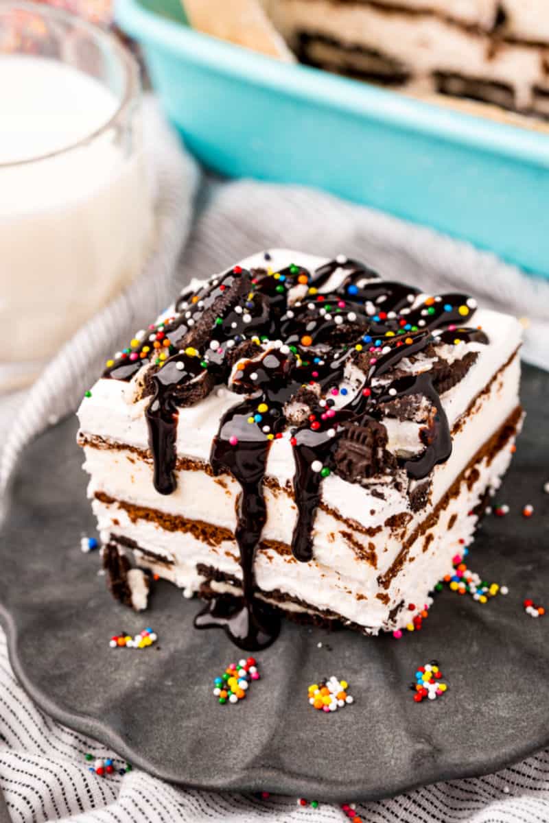 slice of oreo ice cream sandwich cake on a plate next to the baking dish and a glass of milk