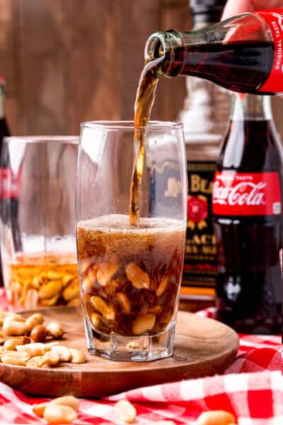 coca cola being poured into a glass with peanut and bourbon
