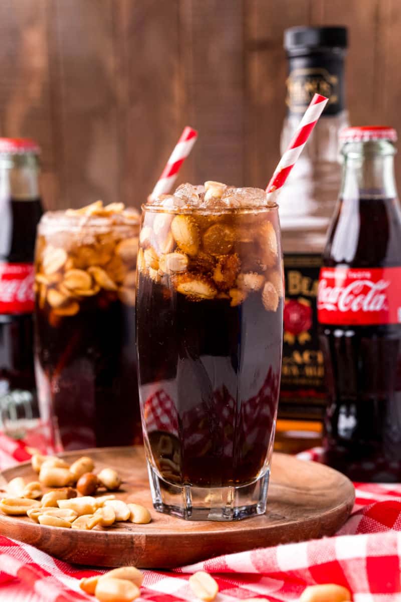 two glasses of peanuts and coke in front of glass coke bottles and a bottle of Jim Beam
