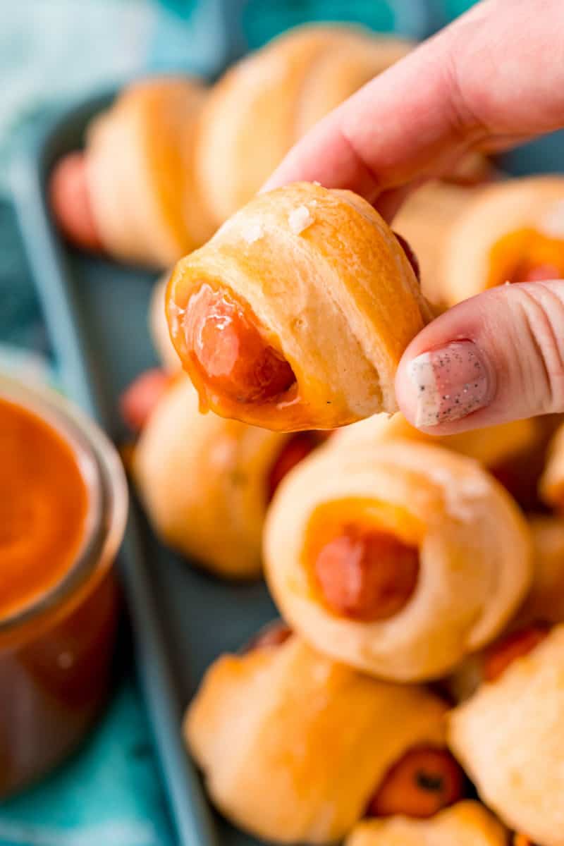 hand holding a cheddar pig in a blanket after dipping it in sauce