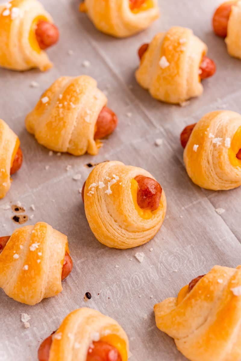 close up of cheddar pigs in a blanket on a baking sheet after cooking