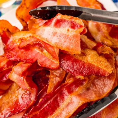 square image of air fryer bacon piled on a plate with tongs