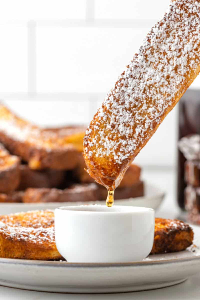 air fryer french toast stick being dipped into syrup