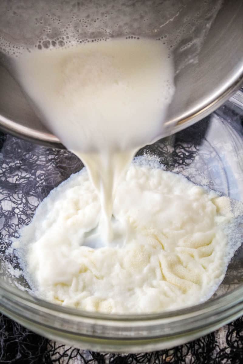 hot milk being poured onto gelatin mixture in a bowl