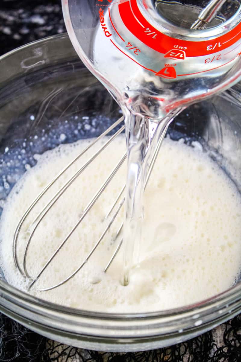 whipped cream vodka being poured into jello mixture in a bowl