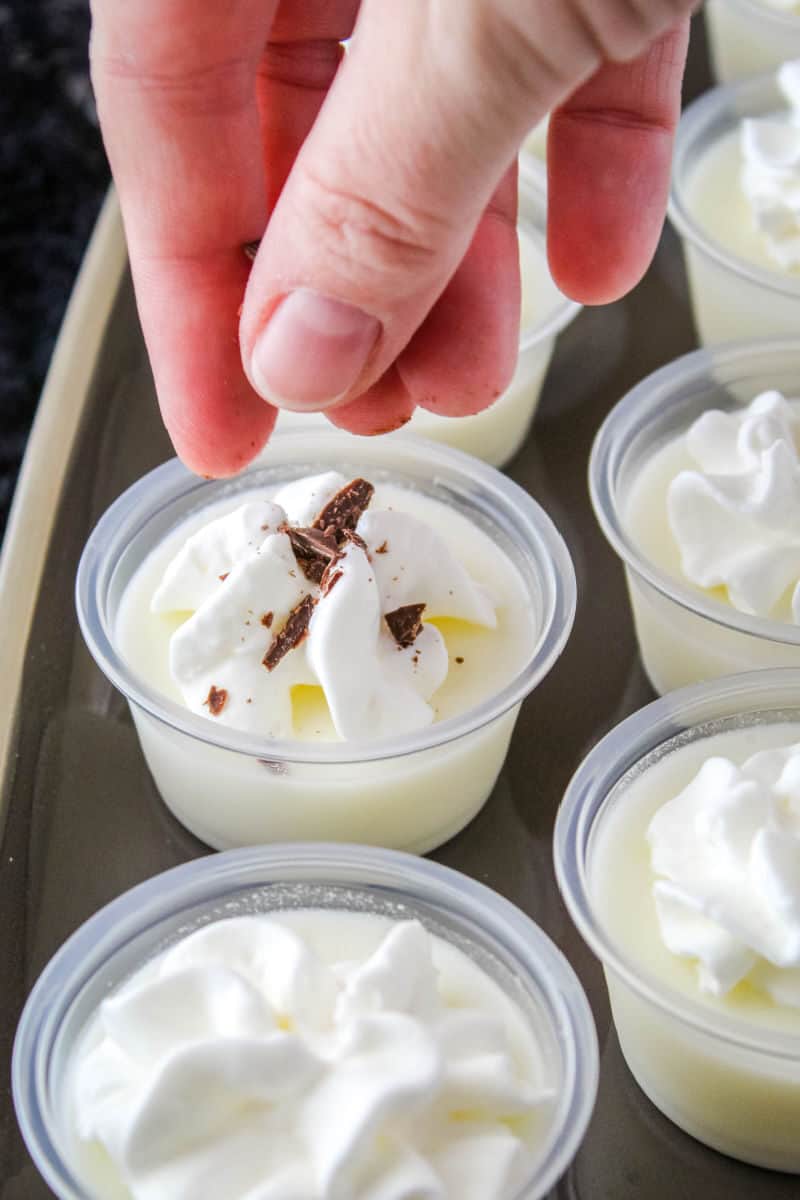 hand sprinkling chocolate shavings over whipped cream vodka jello shots with whipped cream on top