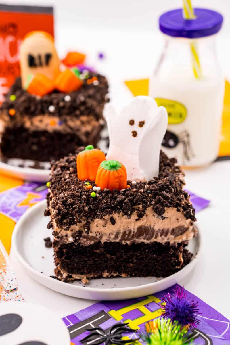 slice of Halloween graveyard chocolate poke cake on a plate with ghost and pumpkins on top