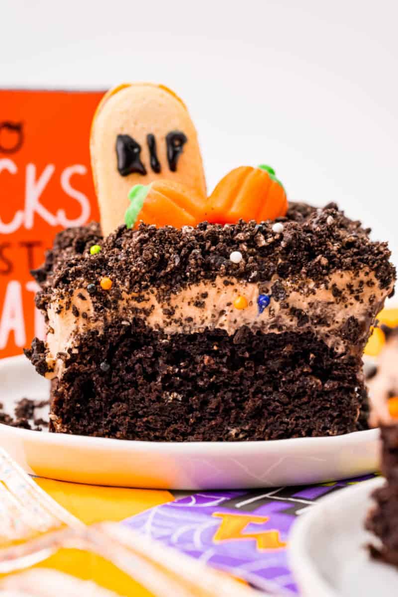 slice of Halloween graveyard chocolate poke cake on a plate to show cake, pudding, and frosting layers