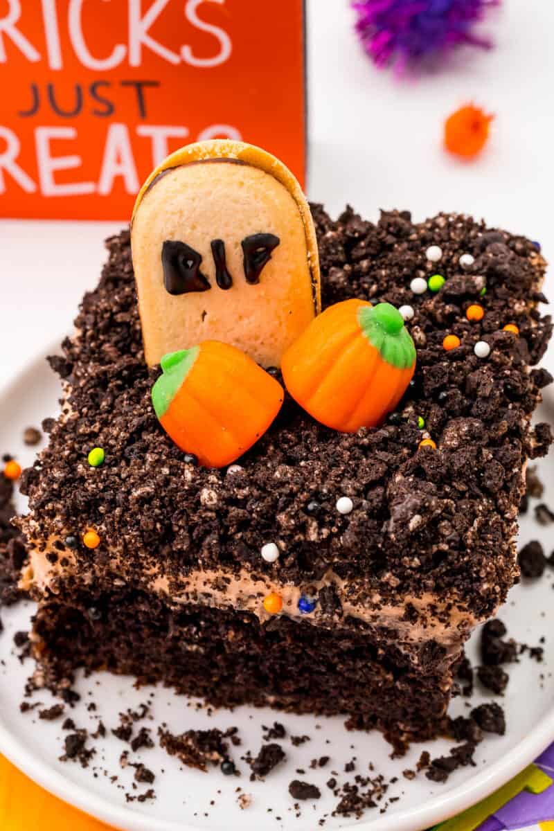 looking down at a slice of Halloween graveyard chocolate poke cake with a tombstone and candy pumpkins on top