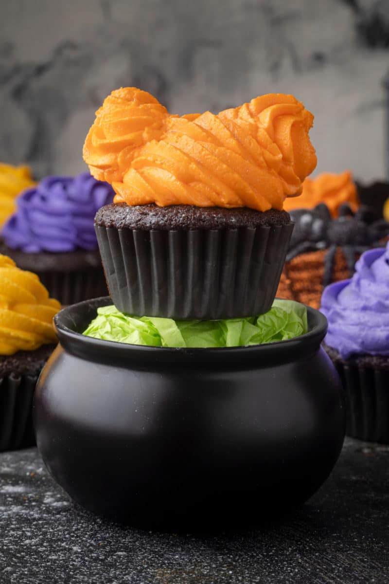 Hocus Pocus chocolate cupcakes for Halloween with one on a plastic cauldron filled with green tissue paper