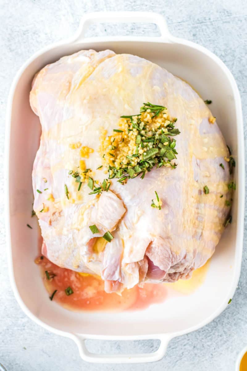 turkey breast in a bakign dish with butter, galric, and herbs rubbed all over