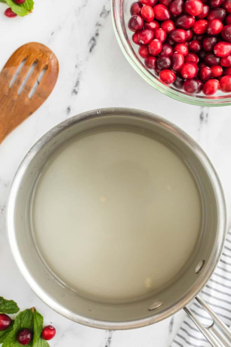 sugar and water in a saucepan next to a bowl of cranberries