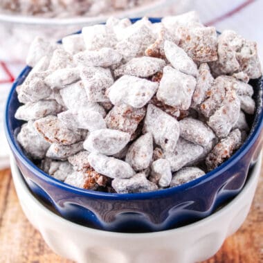 square image of puppy chow muddy buddies in a bolue bowl stacked on a white bowl