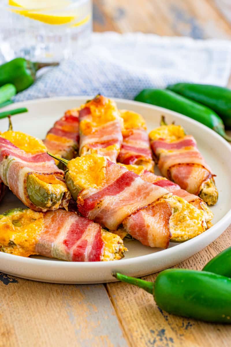 plate of bacon wrapped jalapeno poppers with fresh jalapenos all around