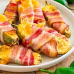 square close up of bacon wrapped jalapeno poppers on a white plate