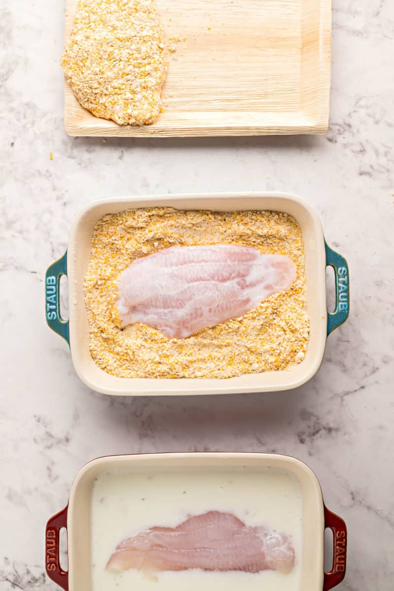 catfish fillets being dredged in buttermilk, seasoned cornmeal, and then set on a tray