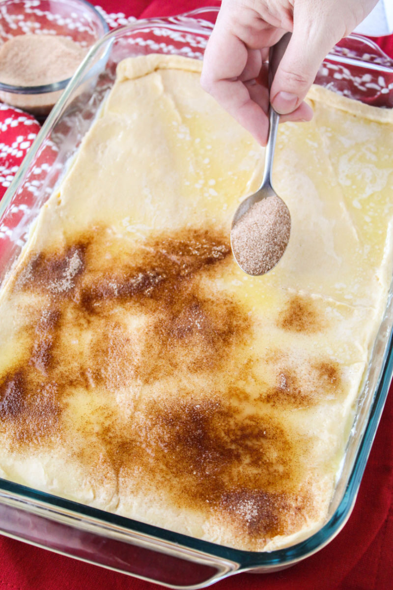 cinnamon-sugar being sprainkled over melted butter on the top layer of crescent roll dough