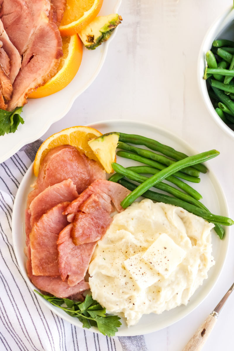 plate of instant pot ham slices with green beans, mashed potatoes, and fruit