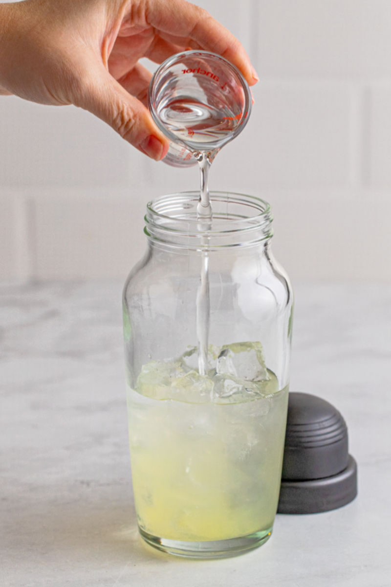 vodka being poured into a cocktail shaker with lemon juice