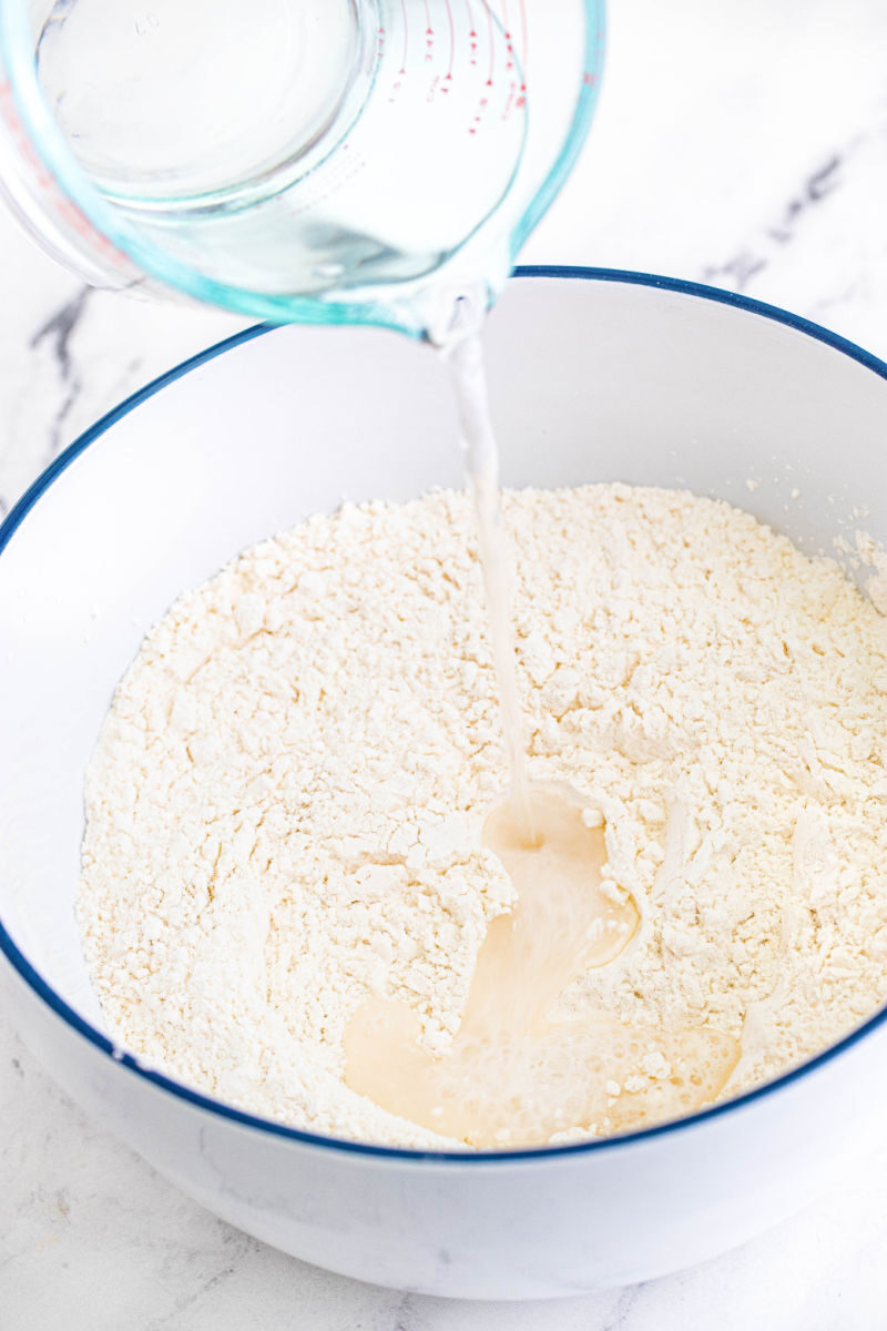 water being poured in a bowl with flour, salt, and yeast