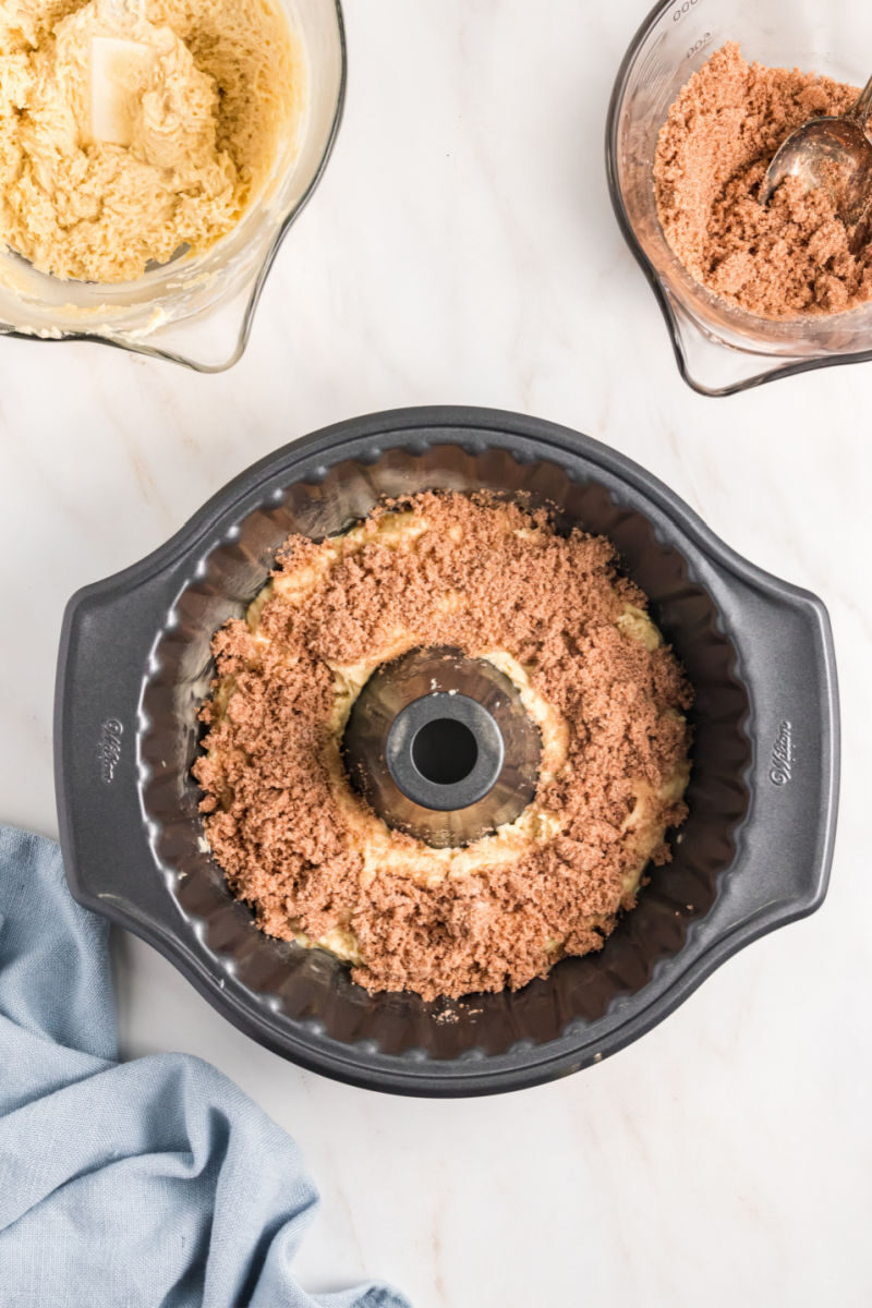 sour cream coffee cake batter in a bundt cake pan with cinnamon sugar filling sprinkled on top