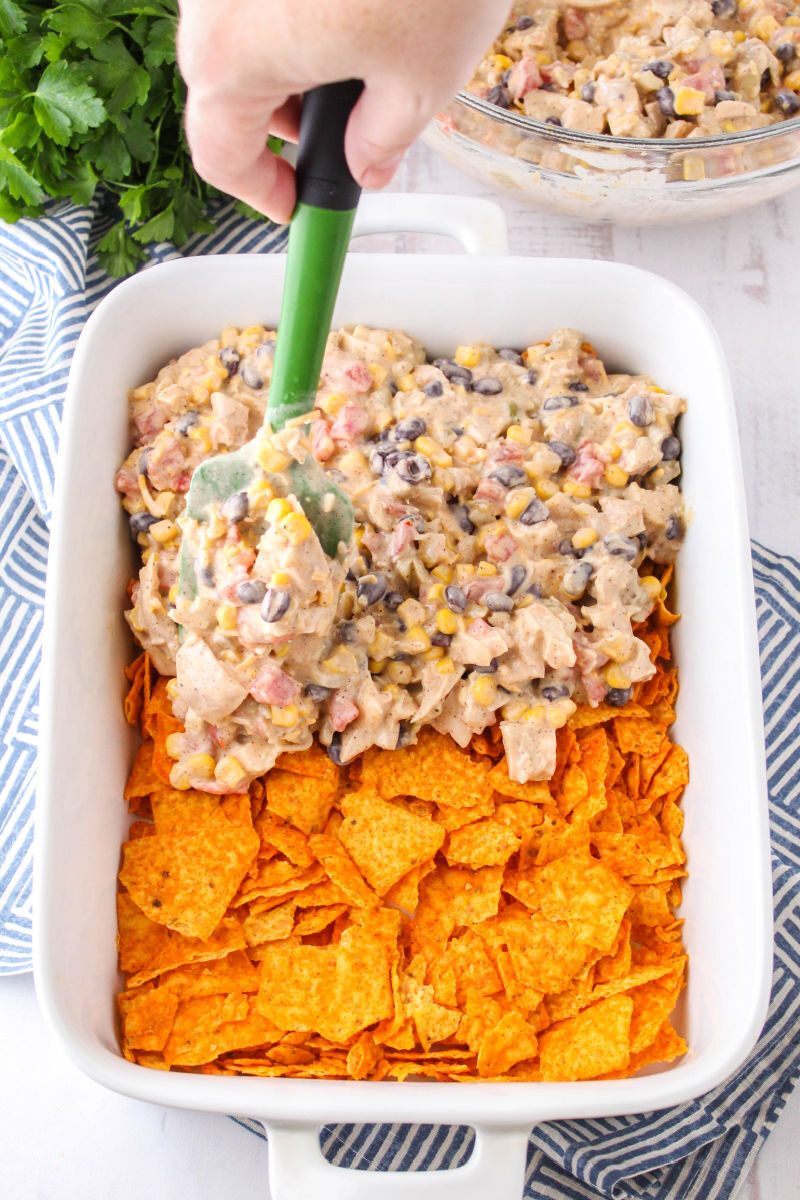 chicken filling being spread over crushed nacho cheese doritos in a baking dish