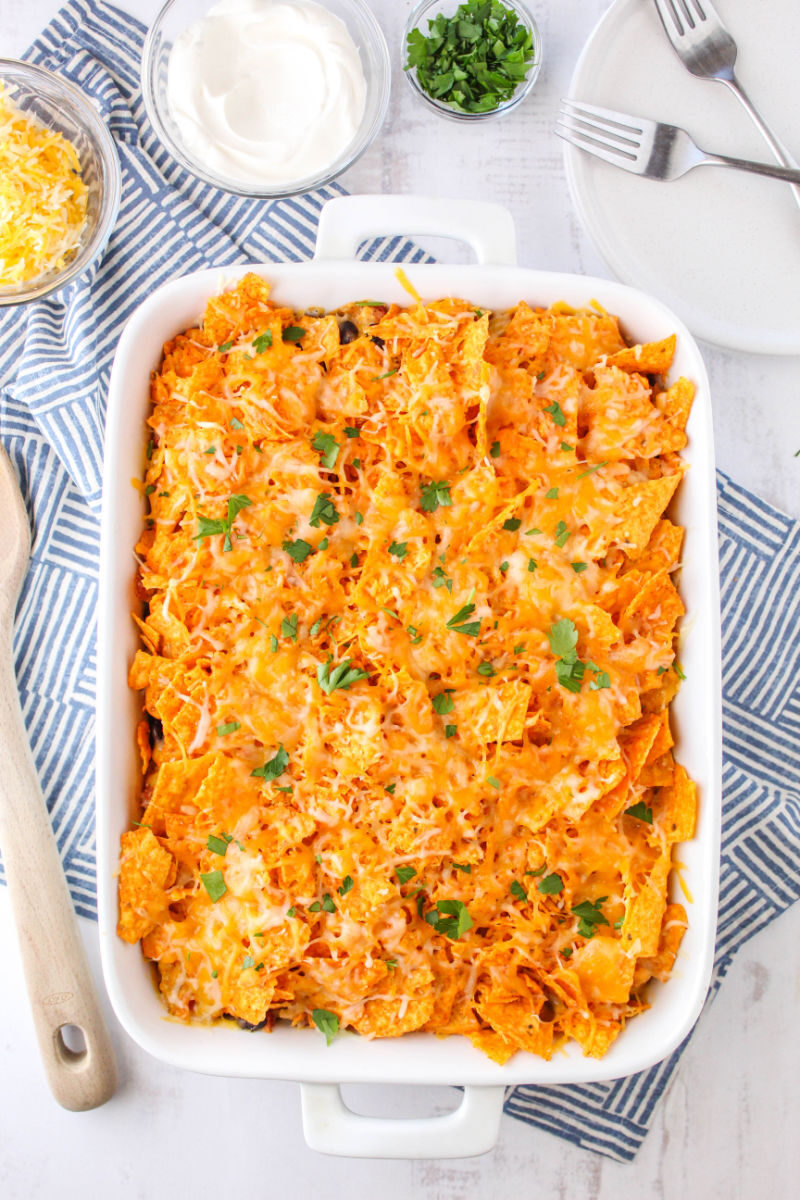 baked dorito casserole in a bakign dish with melted cheese and chopped parsley on top