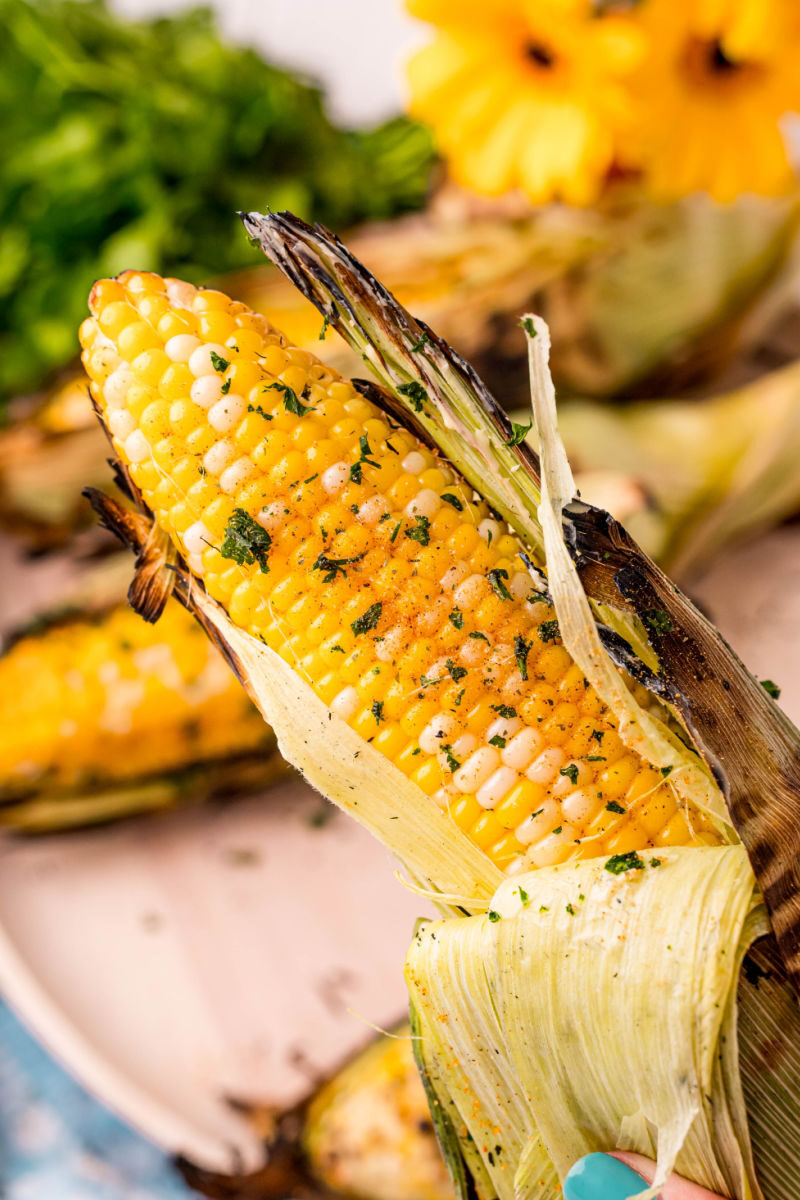 hand holding a grille corn on the cob with butter, salt and pepper