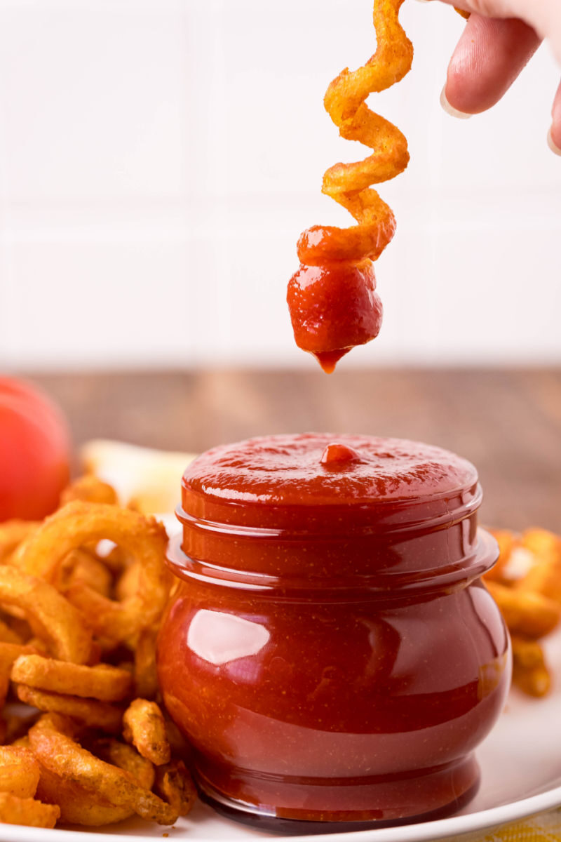 curly fry over a jar of homemade ketchup after being dipped