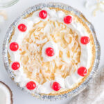 square image of a pina colada pie topped with toasted coconut, whipped cream, and cherries