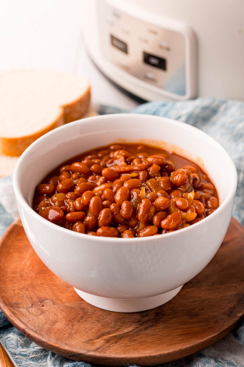 bowl of crockpot baked beans with a slow cooker and bread slices in the background