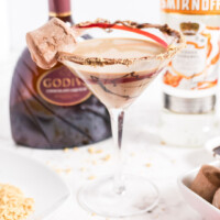 square image of a caramel s'more martini in from of a caramel vodka and chocolate liqueur bottle