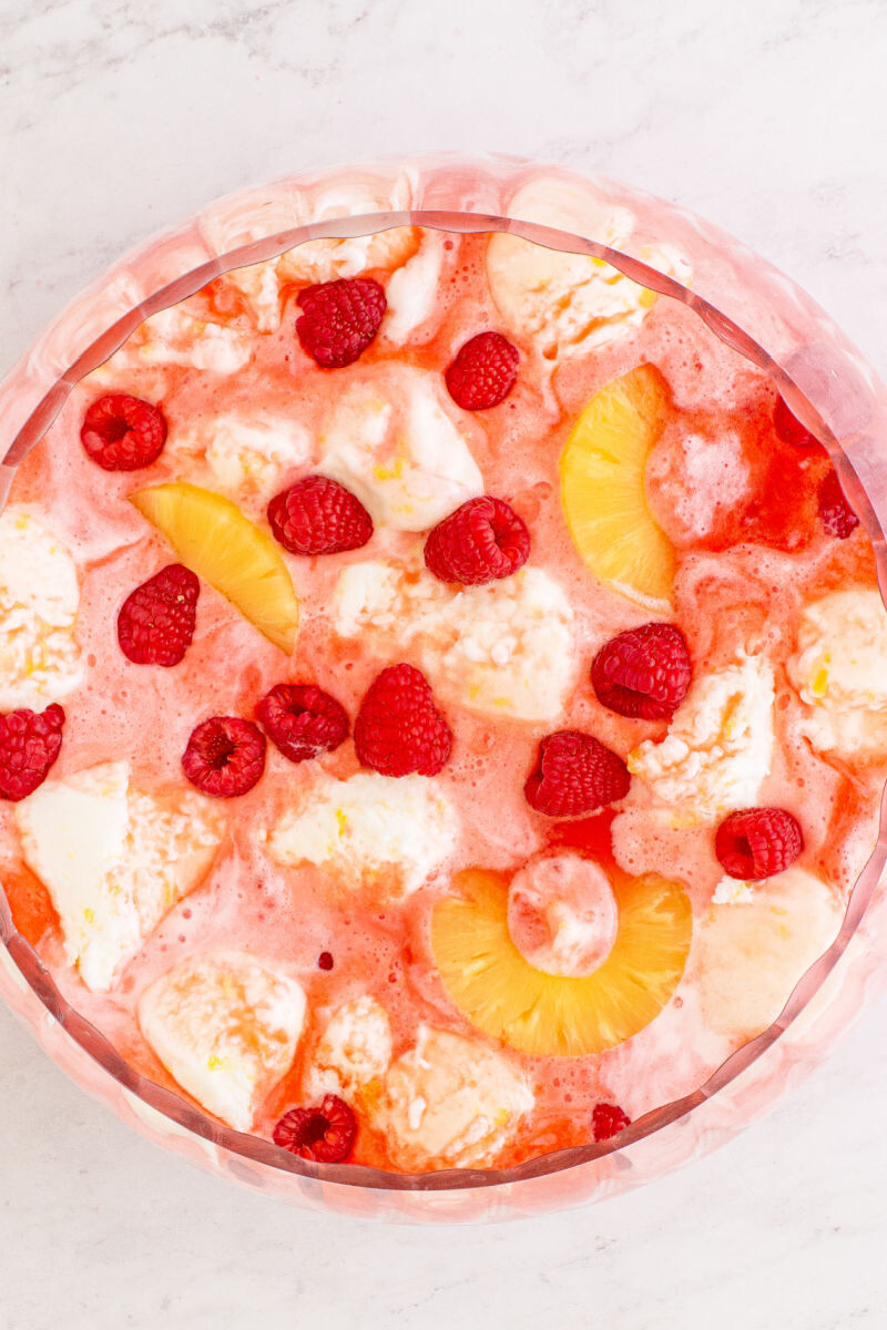 boozy sherbet punch with pineapple slices an raspberries in the punch bowl