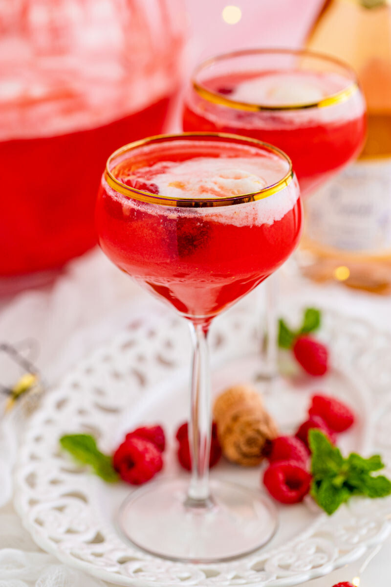 two glasses of boozy sherbet punch with a scoop of sherbet and raspberries