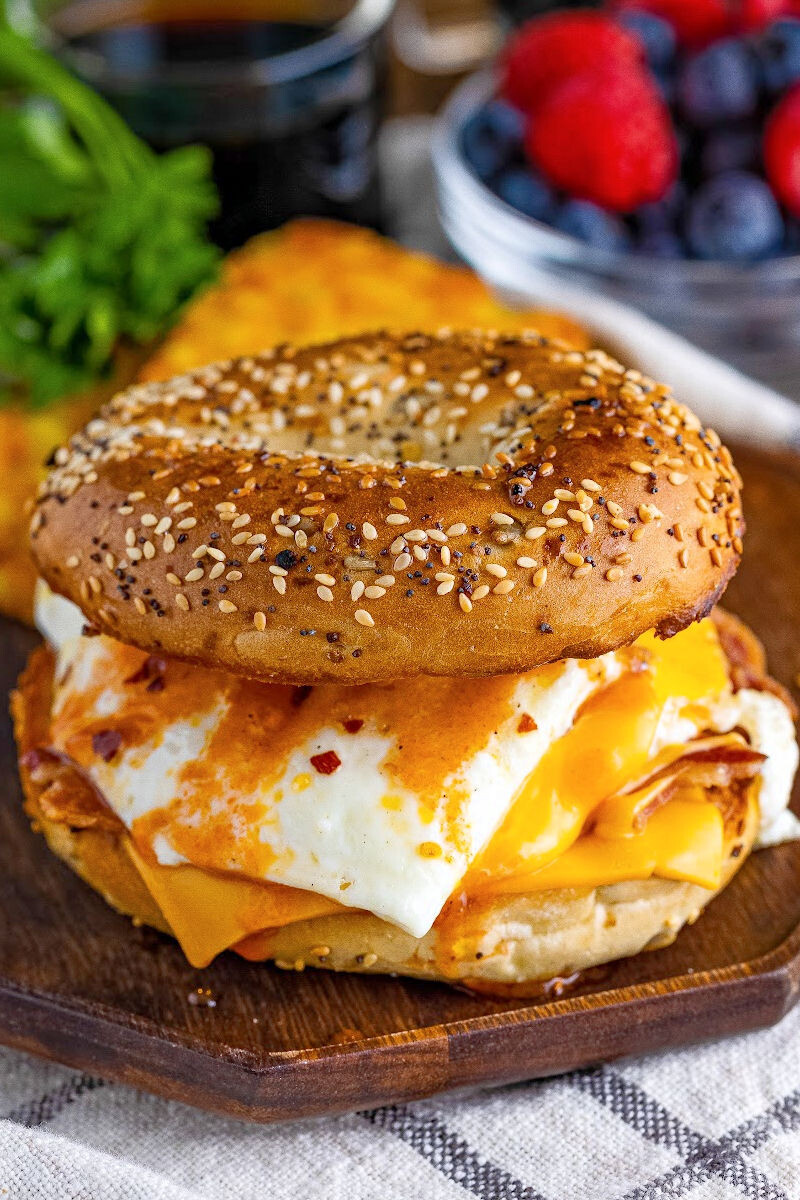 bacon, egg & cheese bagel breakfast sandwich with hot sauce on a wooden plate