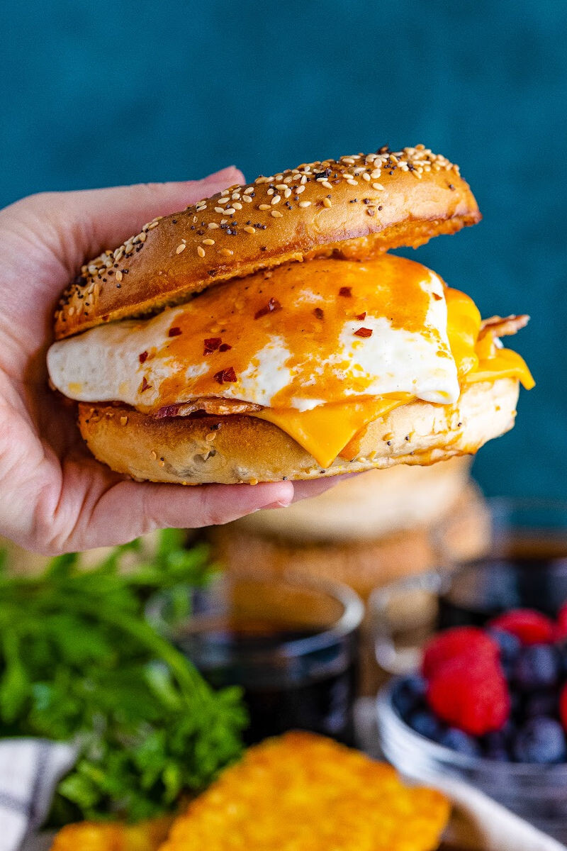 hand holding a bacon, egg & cheese bagel breakfast sandwich