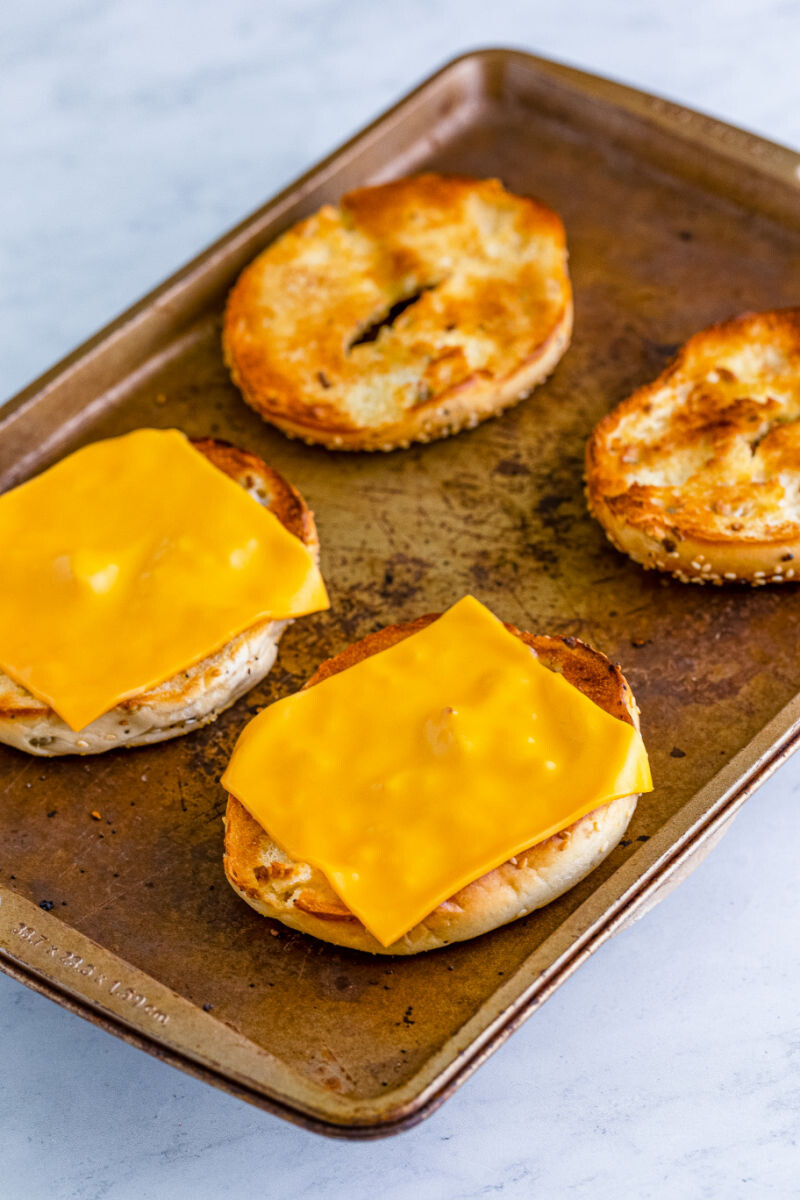 toasted bagel halves on a baking sheet with slices of cheese on the bottoms