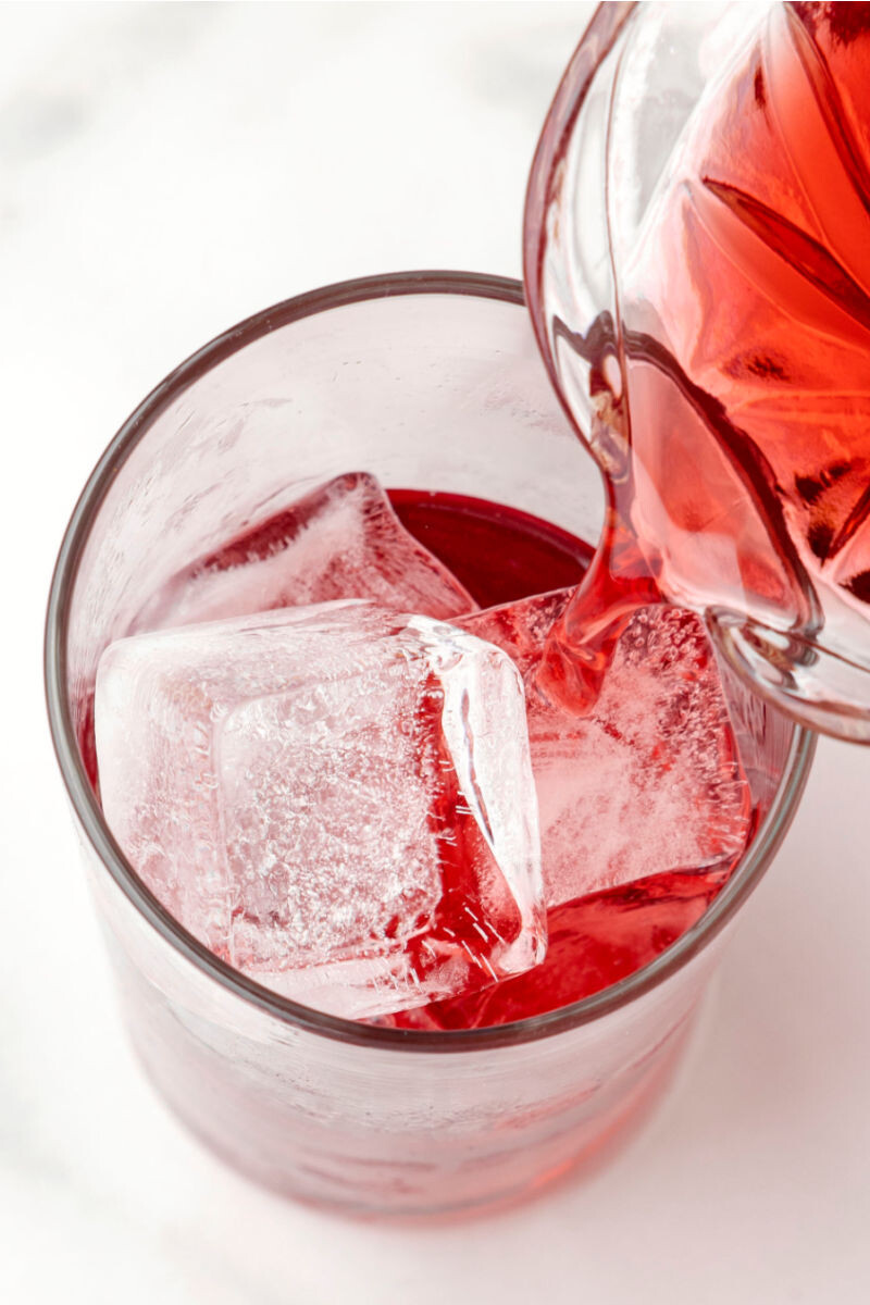 cranberry juice being poured into a glass with ice and vodka