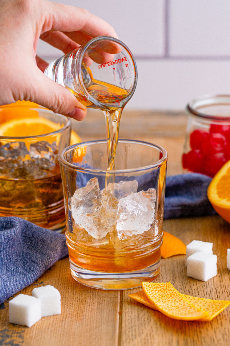 bourbon being poured over ice in a glass with muddled sugar and bitters