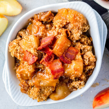 square image of bacon apple crisp in a white bowl with bacon on top