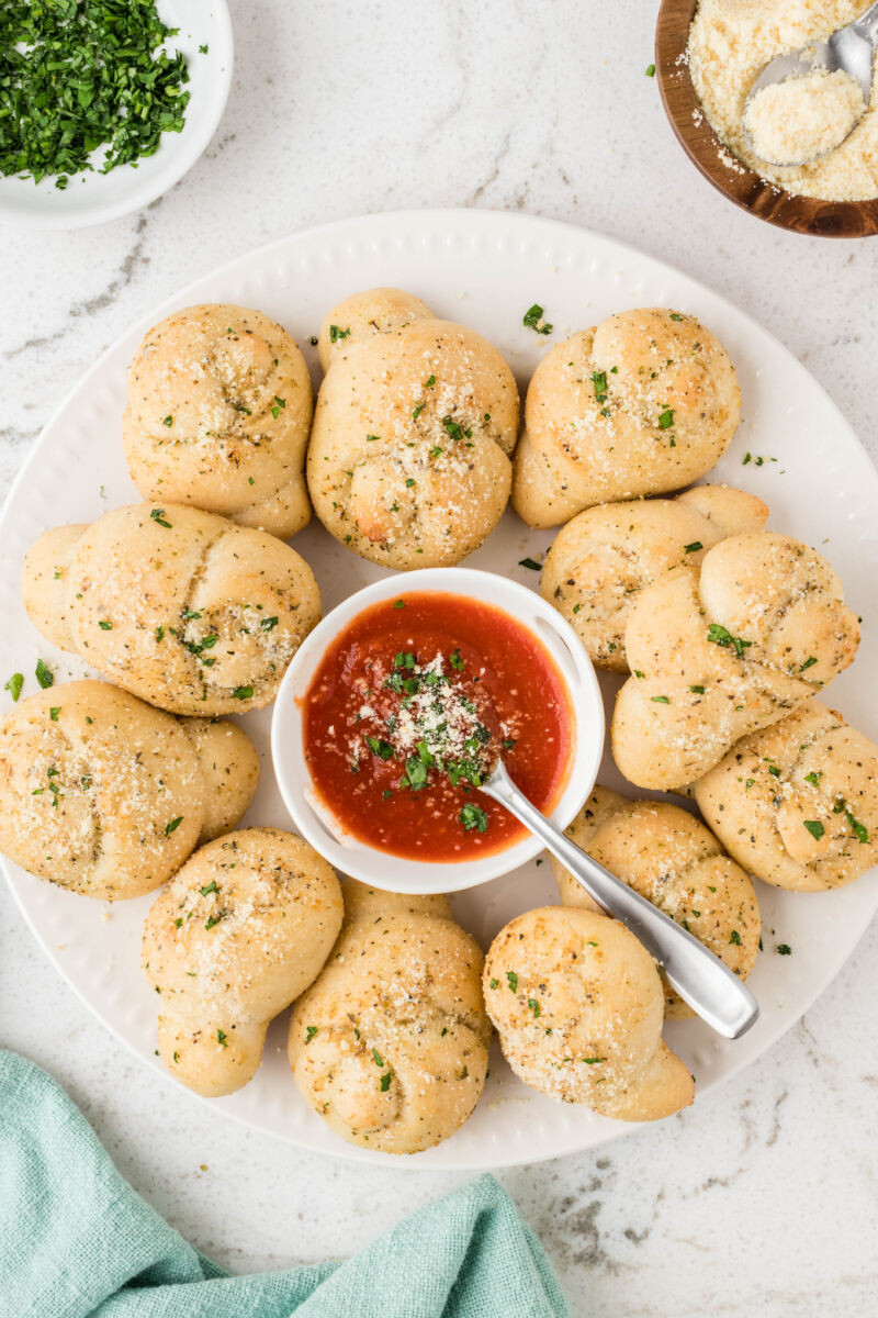garlic knots on a plate with a bowl of marinara in the center
