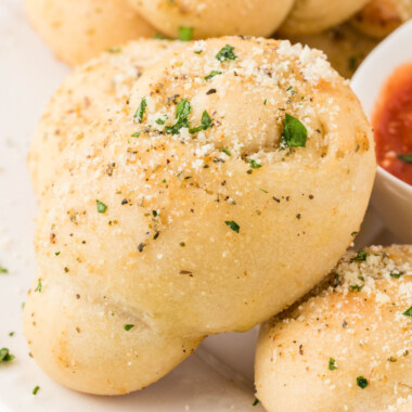 square close up of image of a garlic knot leaning against a bowl of marinara