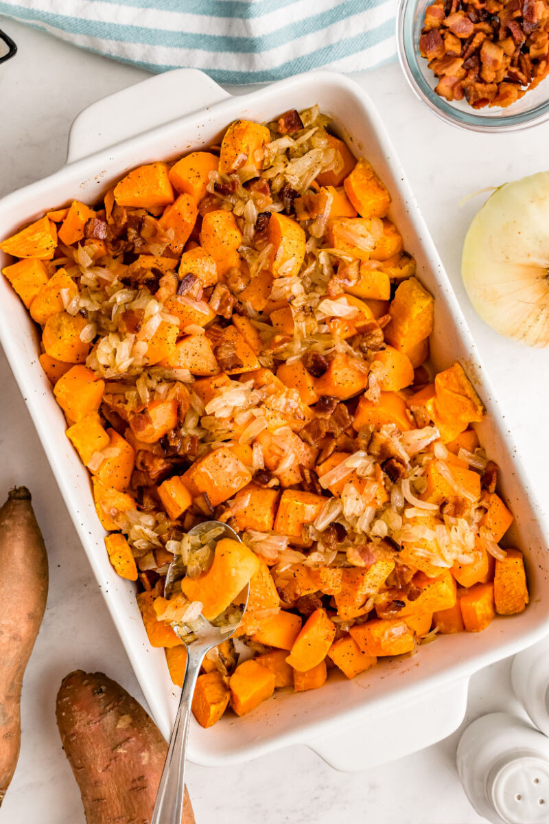 maple glazed sweet potatoes with bacon in a baking dish with a serving spoon